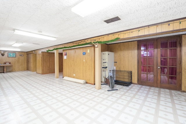 basement featuring french doors, a textured ceiling, and wooden walls