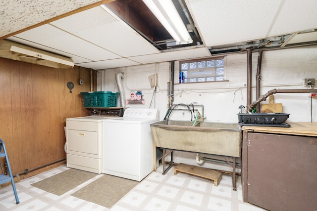 clothes washing area with separate washer and dryer, wooden walls, and sink