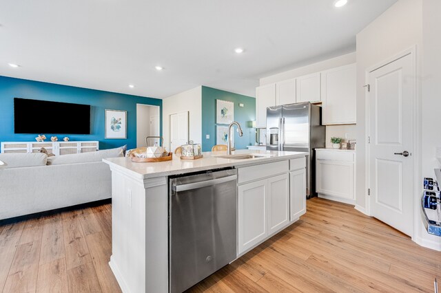 kitchen featuring sink, light stone counters, stainless steel dishwasher, light hardwood / wood-style floors, and a kitchen island with sink