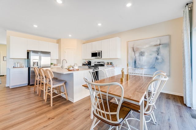 kitchen featuring stainless steel appliances, an island with sink, light wood-style flooring, and white cabinetry