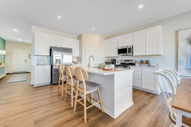 kitchen featuring stainless steel appliances, an island with sink, light wood-style floors, and light countertops