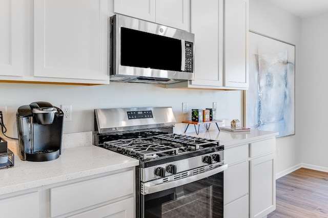 kitchen with appliances with stainless steel finishes, light wood-type flooring, white cabinets, and light stone counters