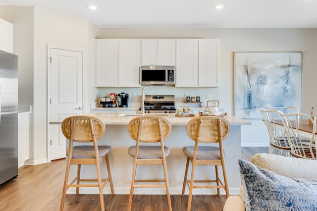 kitchen with a breakfast bar, white cabinetry, light countertops, light wood-style floors, and appliances with stainless steel finishes