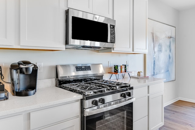 kitchen with light wood-style flooring, white cabinets, appliances with stainless steel finishes, and light stone countertops