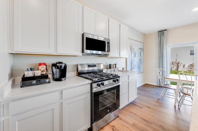 kitchen with baseboards, white cabinets, light stone countertops, light wood-style floors, and appliances with stainless steel finishes