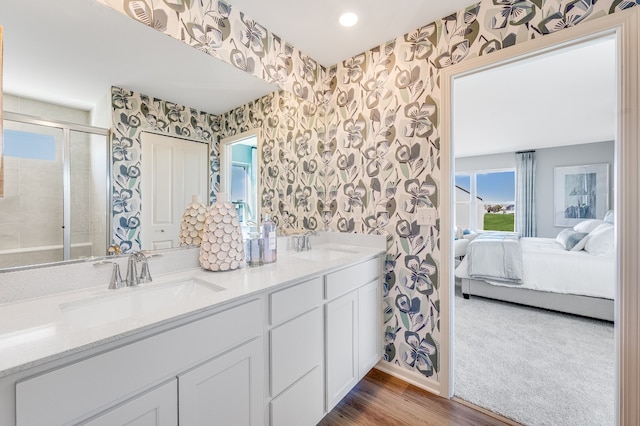 ensuite bathroom featuring a tile shower, a sink, and wallpapered walls