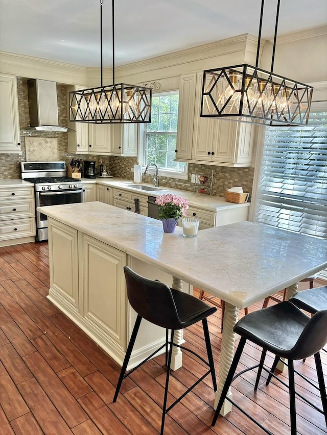 kitchen with decorative light fixtures, gas stove, wall chimney range hood, and sink