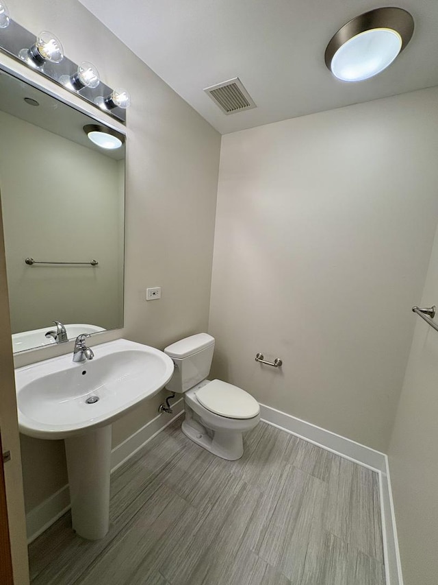 half bathroom with toilet, baseboards, wood finished floors, and a sink