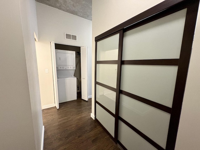 hallway featuring stacked washing machine and dryer, dark wood-type flooring, and baseboards