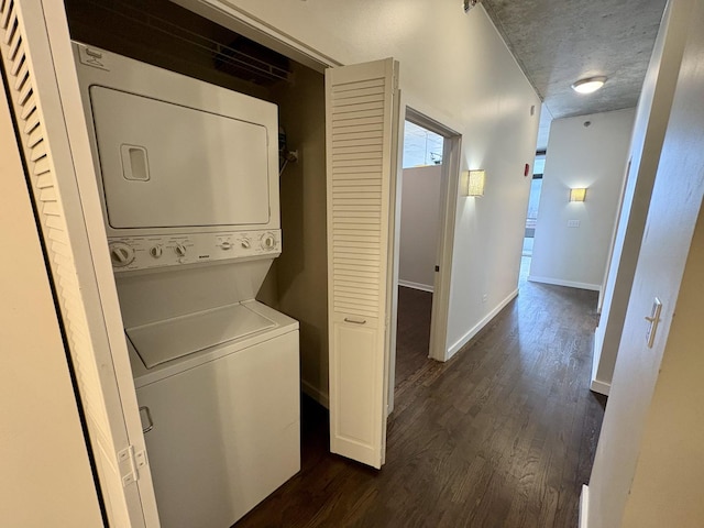washroom featuring stacked washer / drying machine, dark wood-type flooring, and baseboards