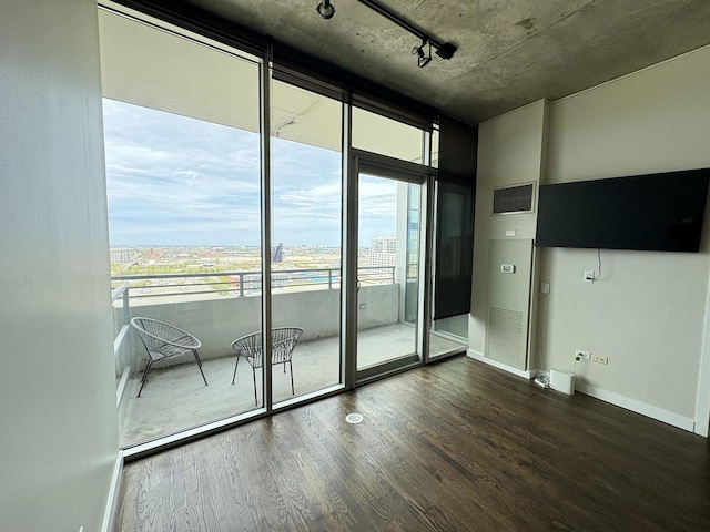 unfurnished room featuring wood finished floors, a wall of windows, baseboards, and rail lighting