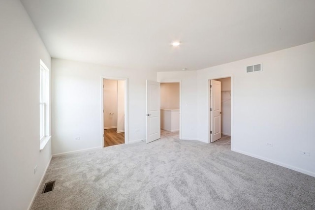 unfurnished bedroom with a walk in closet, light carpet, connected bathroom, and a closet