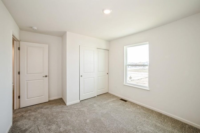 unfurnished bedroom with light colored carpet and a closet