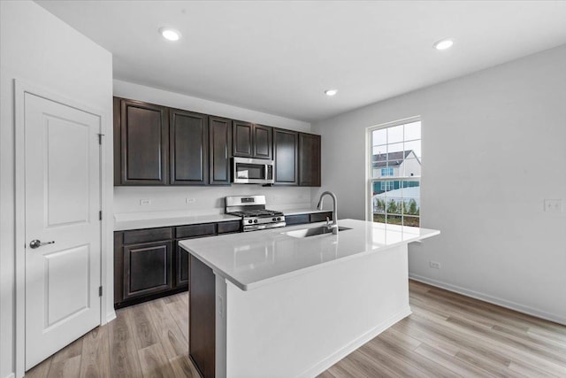 kitchen featuring sink, an island with sink, dark brown cabinets, light hardwood / wood-style floors, and stainless steel appliances