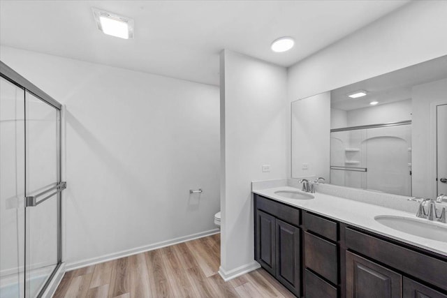 bathroom featuring wood-type flooring, vanity, toilet, and a shower with shower door