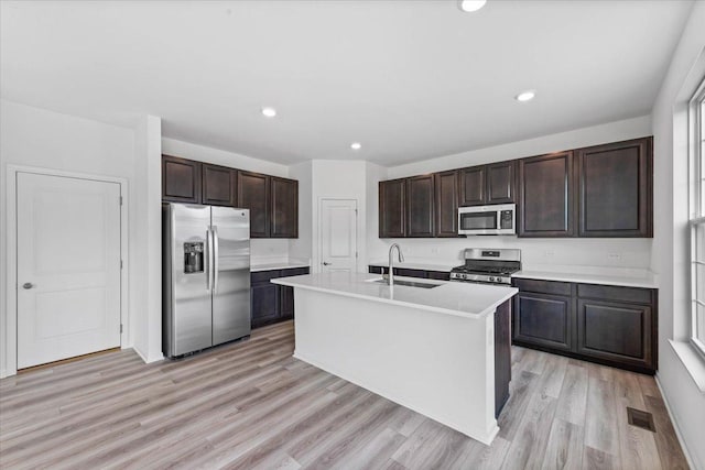 kitchen with dark brown cabinetry, sink, stainless steel appliances, light hardwood / wood-style flooring, and a center island with sink