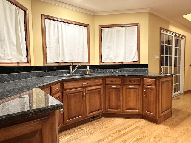 bar with ornamental molding, light hardwood / wood-style flooring, dark stone counters, and sink