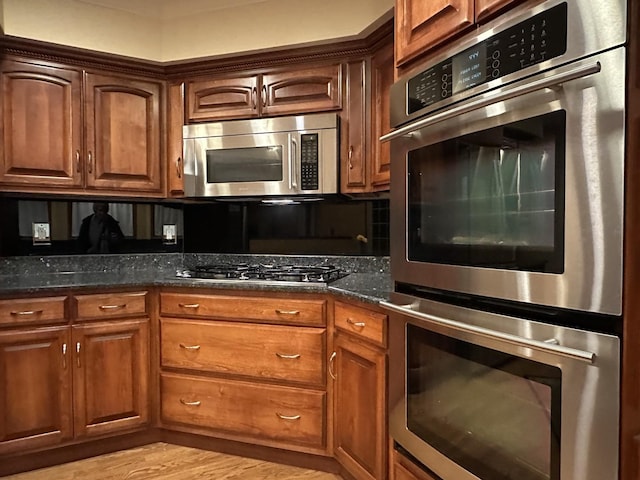 kitchen with stainless steel appliances, light hardwood / wood-style flooring, and dark stone countertops