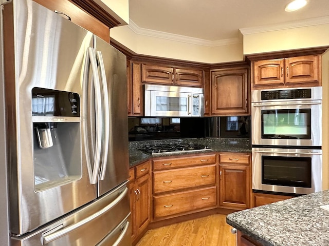 kitchen featuring dark stone counters, stainless steel appliances, light hardwood / wood-style flooring, and crown molding