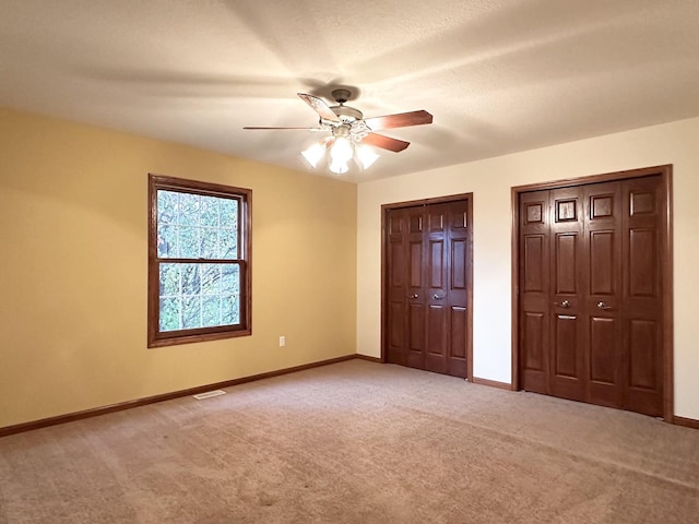 unfurnished bedroom featuring ceiling fan, light colored carpet, a textured ceiling, and two closets