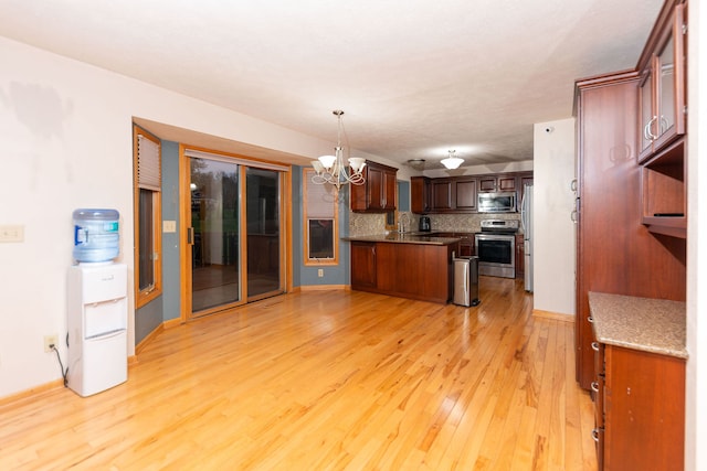 kitchen with backsplash, an inviting chandelier, light wood-type flooring, appliances with stainless steel finishes, and decorative light fixtures