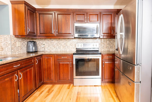 kitchen with light stone countertops, decorative backsplash, stainless steel appliances, and light hardwood / wood-style floors