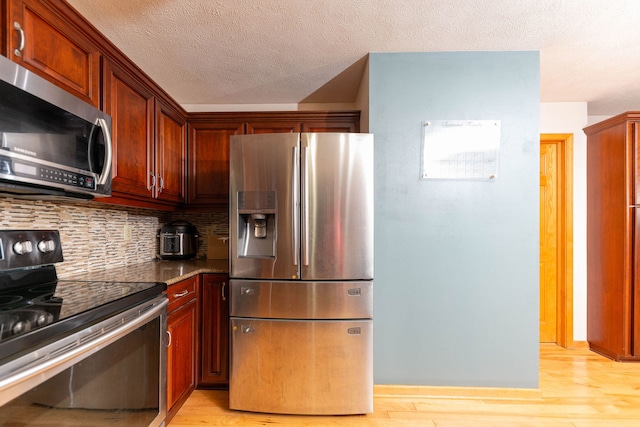 kitchen featuring decorative backsplash, dark stone countertops, a textured ceiling, light hardwood / wood-style floors, and stainless steel appliances