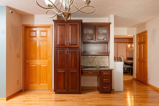 kitchen featuring backsplash, dark stone counters, pendant lighting, light hardwood / wood-style flooring, and a chandelier