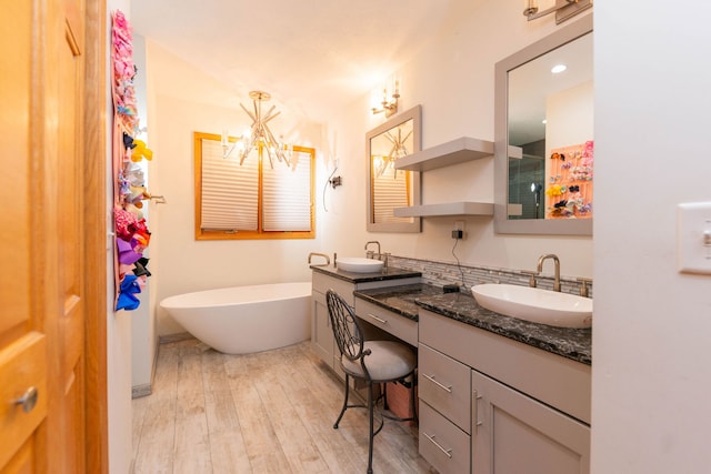 bathroom with a notable chandelier, wood-type flooring, a tub to relax in, and vanity