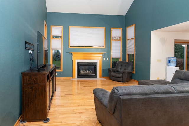 living room featuring a tile fireplace, vaulted ceiling, and light hardwood / wood-style flooring