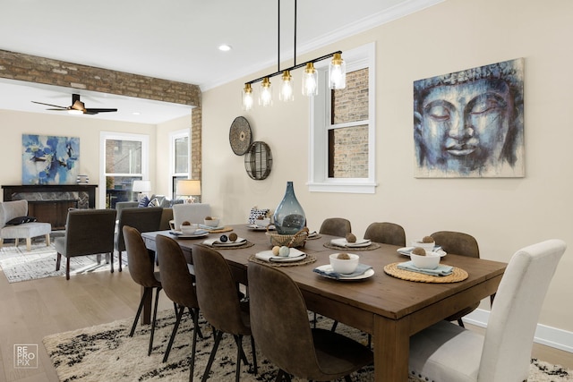 dining room featuring baseboards, a ceiling fan, ornamental molding, wood finished floors, and a fireplace
