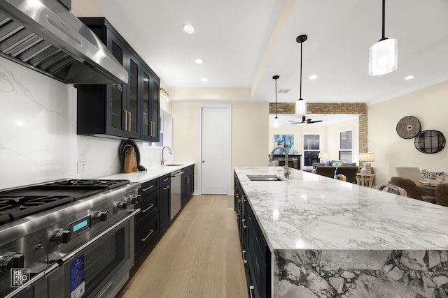 kitchen featuring stainless steel appliances, wall chimney range hood, a sink, and dark cabinets