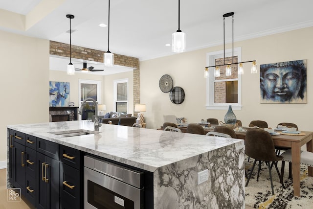 kitchen with a center island with sink, stainless steel microwave, ornamental molding, open floor plan, and a sink