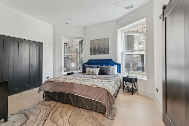 bedroom with a barn door, light hardwood / wood-style flooring, and multiple windows