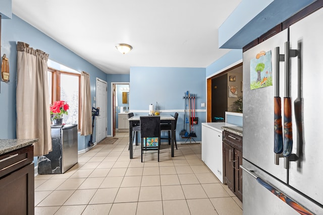 kitchen featuring dark brown cabinets, stainless steel fridge, light tile patterned flooring, and a breakfast bar area