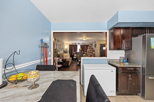 kitchen featuring light tile patterned floors, backsplash, stainless steel refrigerator, and dark brown cabinets