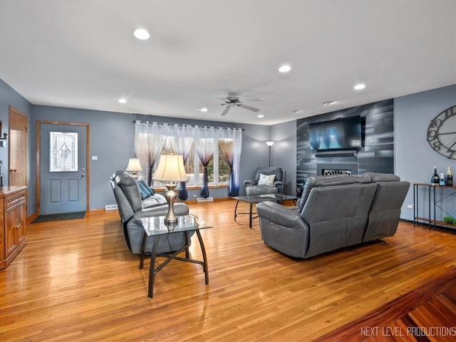 living room featuring a tiled fireplace, ceiling fan, and light wood-type flooring