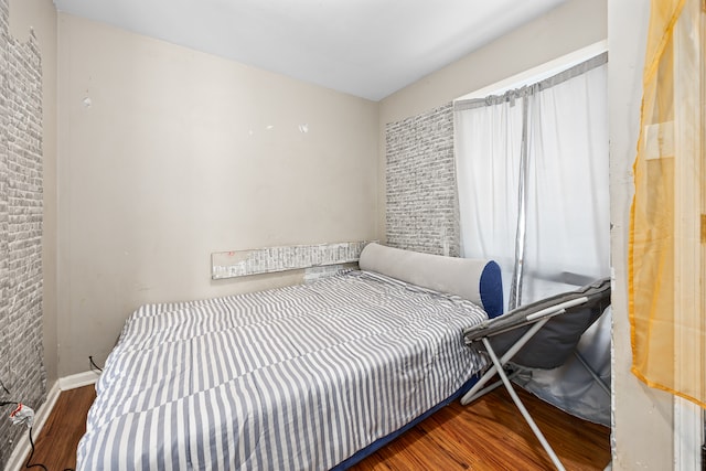 bedroom with dark hardwood / wood-style flooring and brick wall