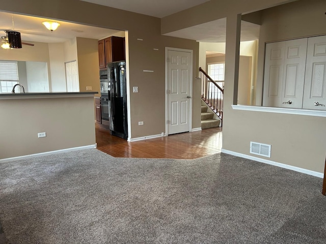 unfurnished living room featuring sink, a healthy amount of sunlight, and dark colored carpet