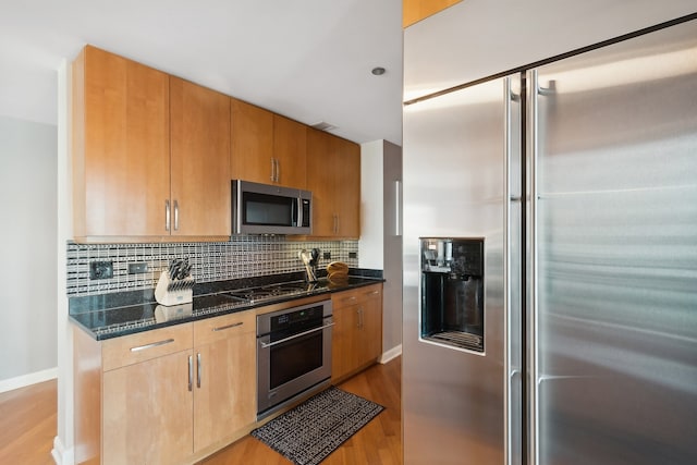 kitchen featuring dark stone counters, stainless steel appliances, tasteful backsplash, and light hardwood / wood-style floors