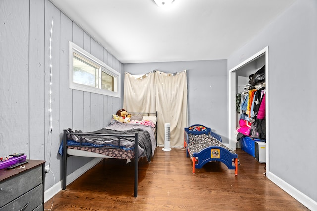 bedroom featuring dark wood-type flooring, wooden walls, and a closet