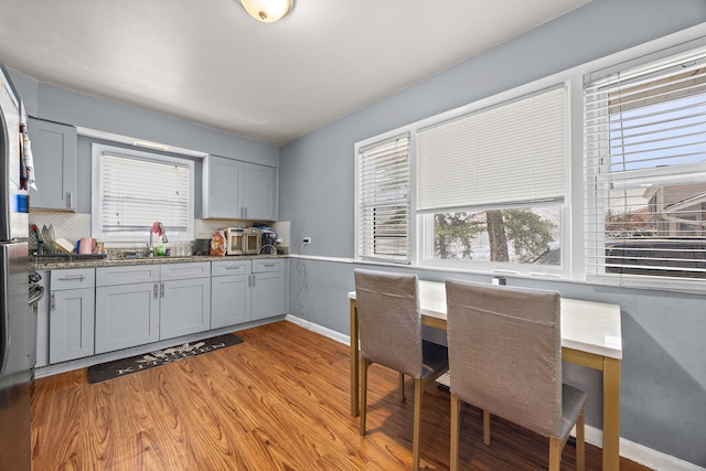 kitchen featuring sink, gray cabinets, dark stone countertops, light wood-type flooring, and tasteful backsplash