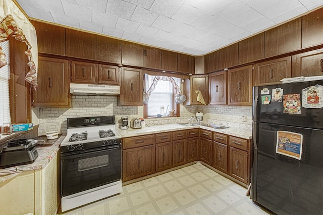 kitchen featuring decorative backsplash, black refrigerator, sink, and white range with gas cooktop