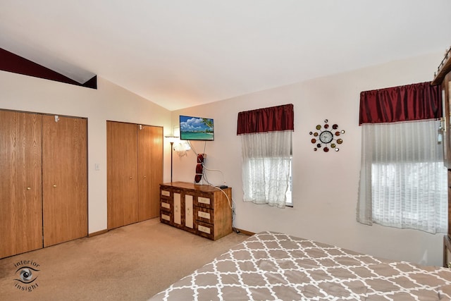 carpeted bedroom featuring two closets and lofted ceiling