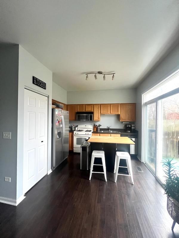 kitchen with stainless steel appliances, a kitchen breakfast bar, dark hardwood / wood-style floors, butcher block countertops, and a kitchen island