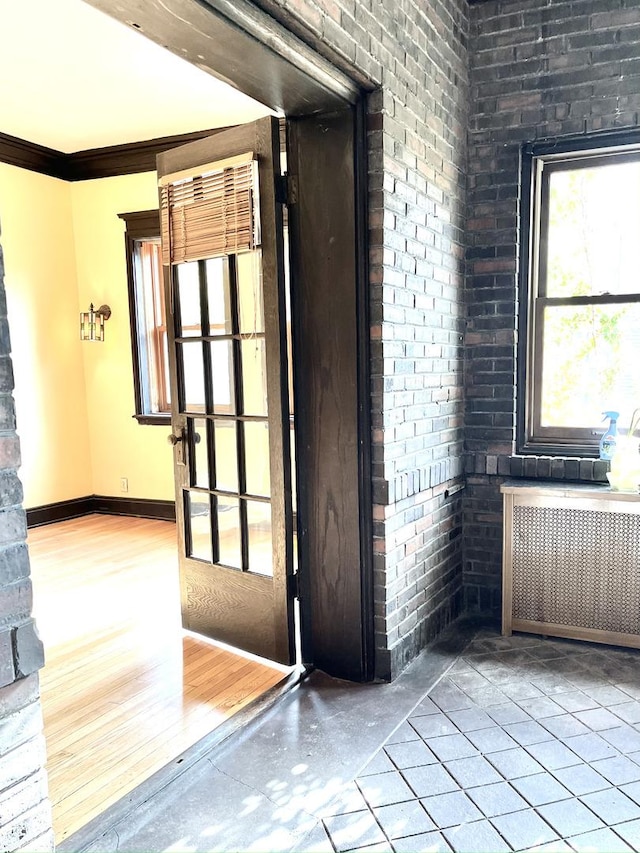 spare room with radiator, wood-type flooring, brick wall, and ornamental molding