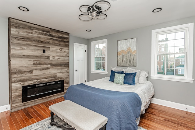 bedroom with multiple windows, wood-type flooring, and a tiled fireplace