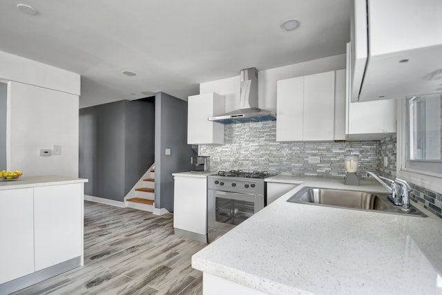 kitchen featuring sink, light hardwood / wood-style flooring, wall chimney exhaust hood, high end stove, and white cabinetry