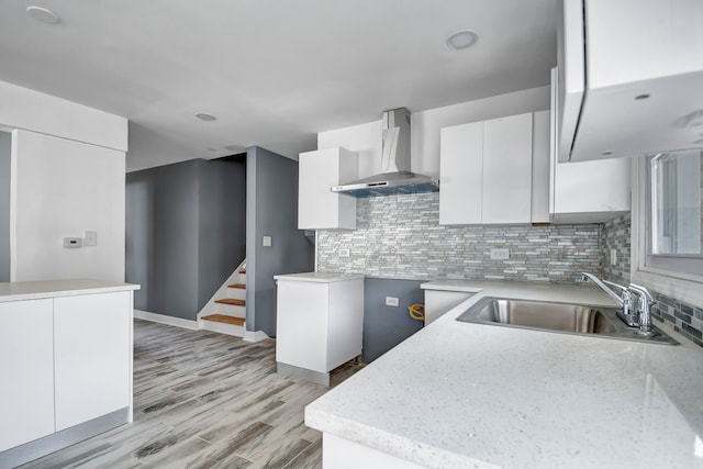 kitchen with wall chimney exhaust hood, white cabinetry, sink, and tasteful backsplash