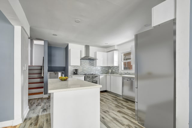 kitchen with wall chimney range hood, light hardwood / wood-style flooring, decorative backsplash, appliances with stainless steel finishes, and white cabinetry